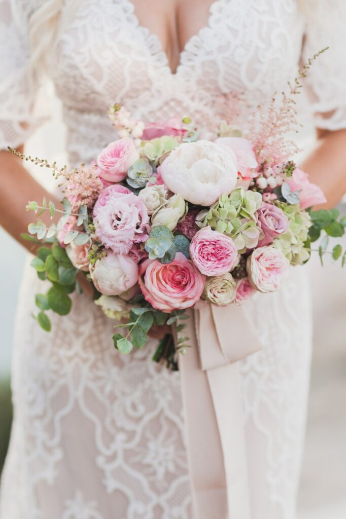 Bride holding in hands small wedding bouquet in pastel colors. Light pink roses and white peony.
