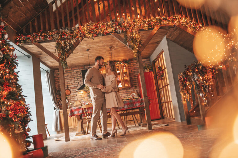 Photo of a couple holding each other in a warm, holiday decorated room.