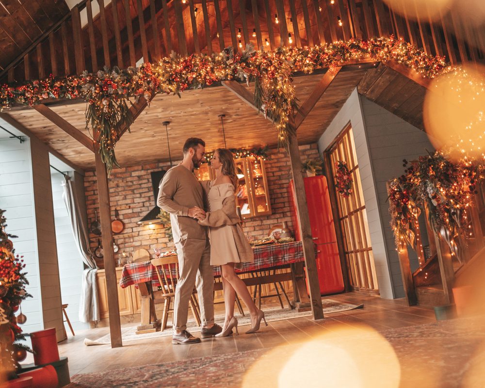 Photo of a couple holding each other in a warm, holiday decorated room.
