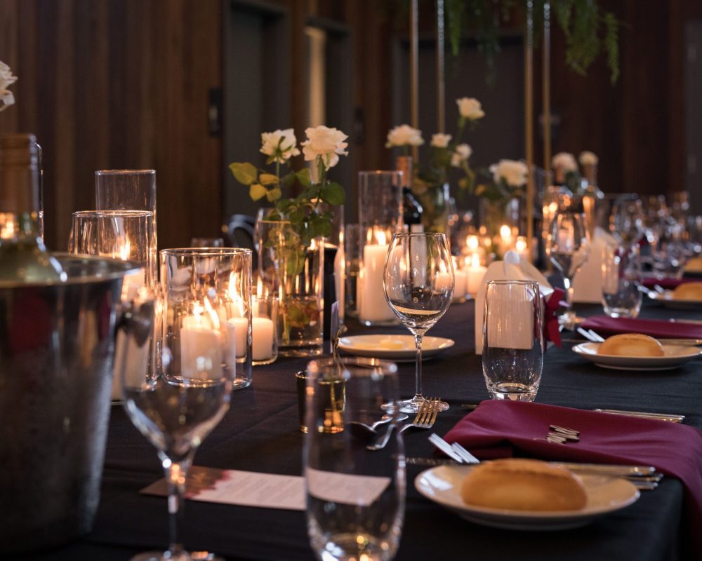 A decorated view of the table setting with candles, white roses, glasses, and a bottle of wine in a bucket