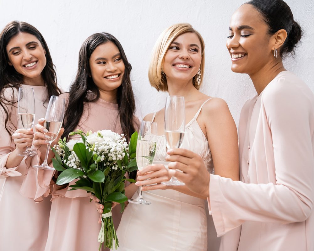 positivity, blonde bride in wedding dress holding bouquet, standing with interracial bridesmaids, champagne glasses, grey background, racial diversity, fashion, multicultural young women
